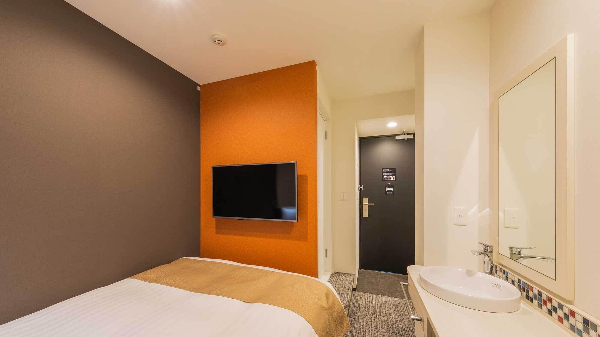 A hotel room with a bed, a mounted TV, a bathroom with a sink and mirror, and a door leading to another room.