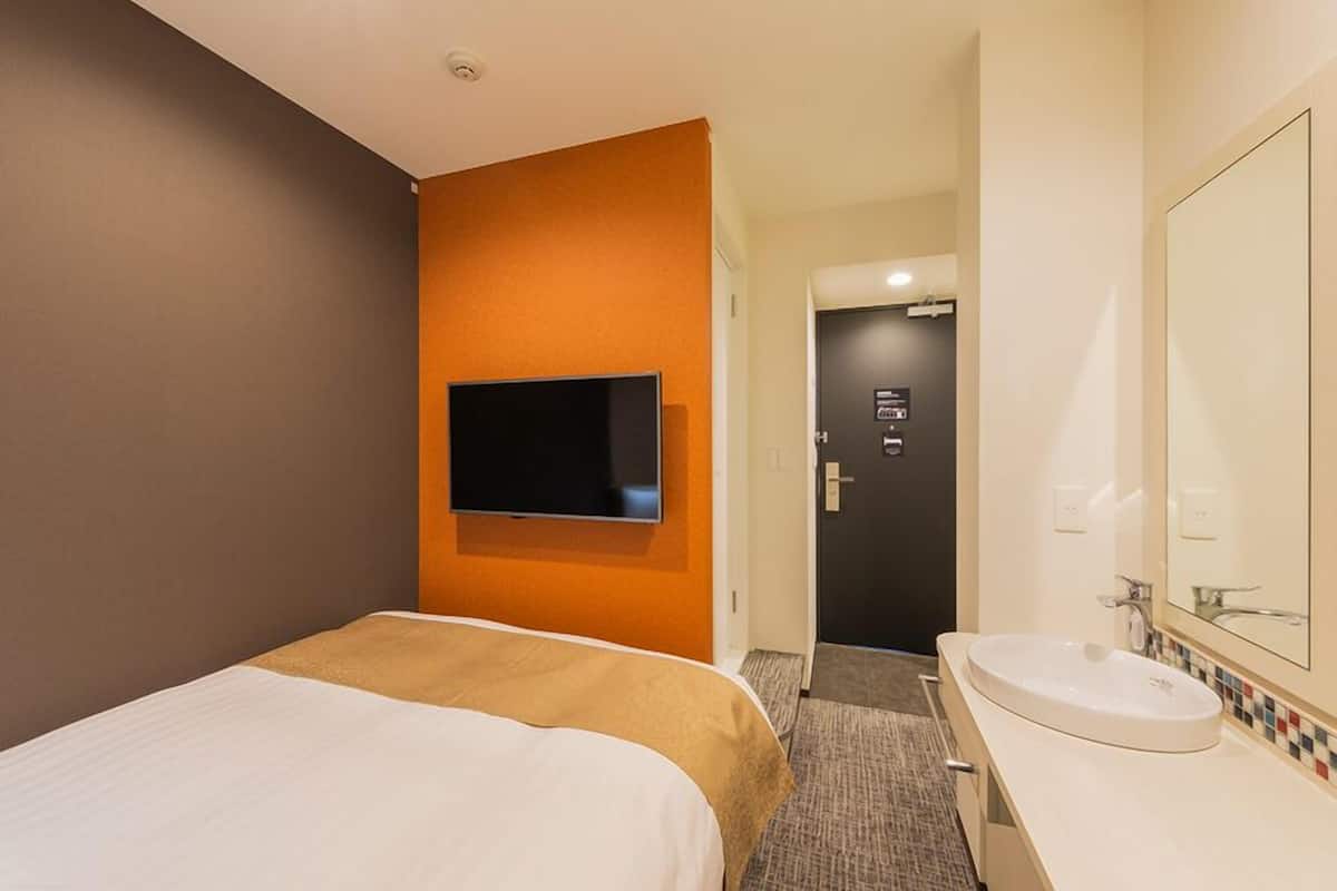 A hotel room with a bed, a television mounted on the wall, a bathroom with a sink and mirror, and a door leading to another room.
