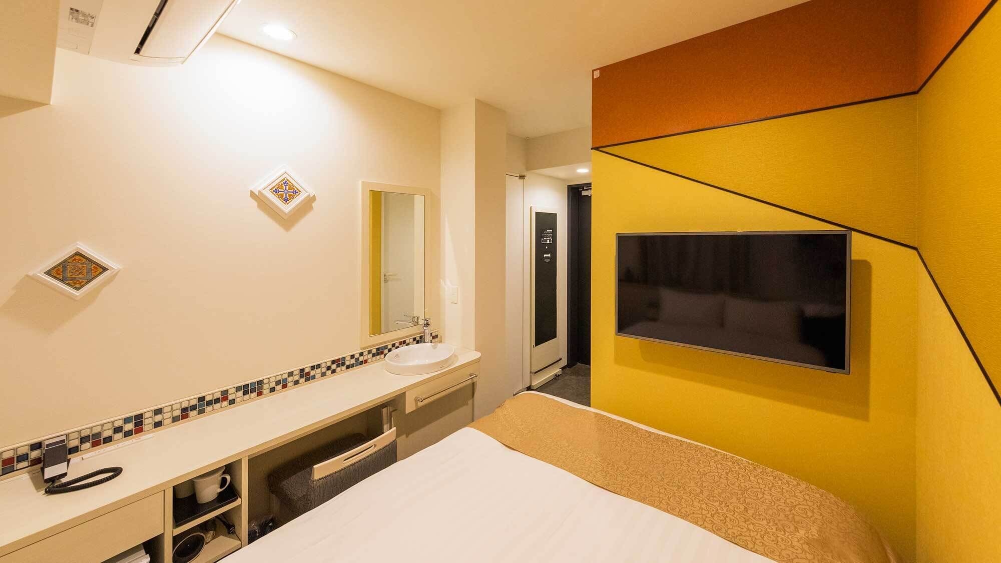 A hotel room with a bed, a bathroom with a sink and mirror, a TV mounted on the wall, and a shower.