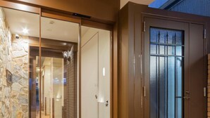A hotel entrance with a stone wall, a sliding glass door, and a metal gate. - Asta Hotel (Tokyo)