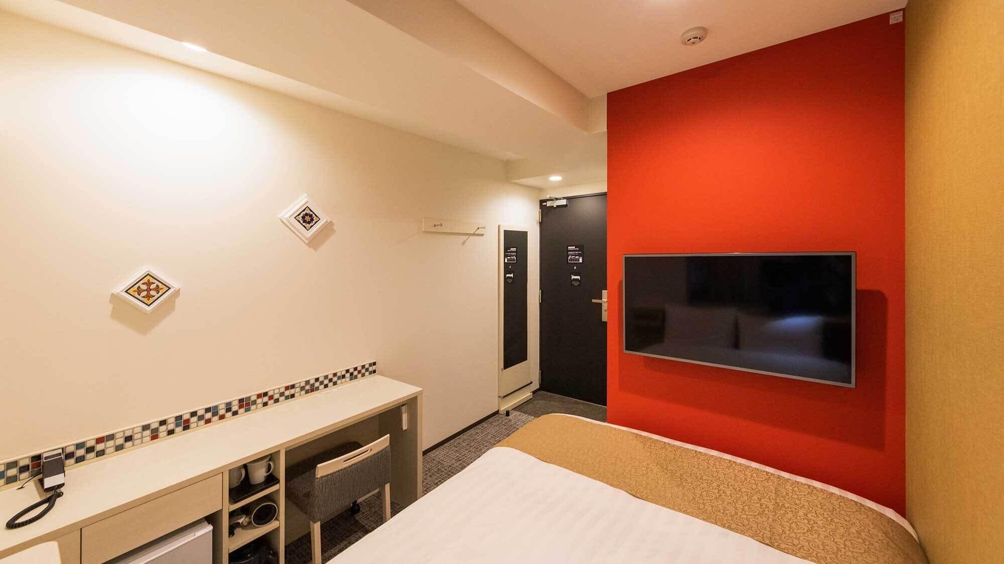 A hotel room with a bed, a desk, a TV, and a red accent wall.