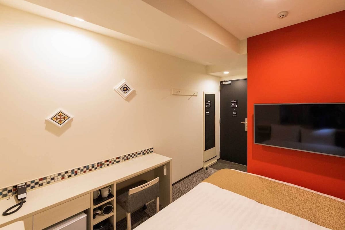 A hotel room with a bed, a desk, a TV, and a red accent wall.