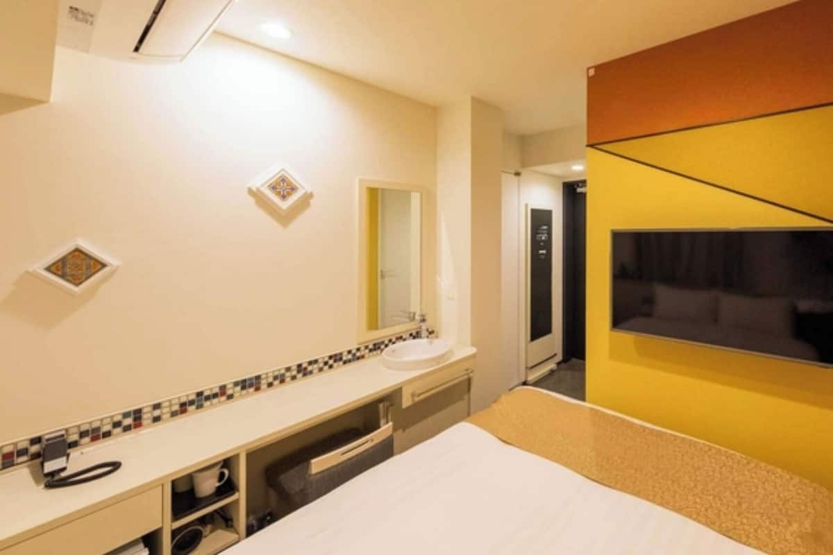 A hotel room with a bed, a bathroom with a sink and mirror, and a TV mounted on the wall.