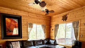 Ein gemütliches Blockhauss-Interieur mit einem Ledersofa, einem Holztisch und einem Deckenventilator.