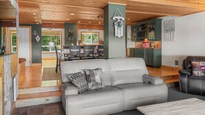A modern living room with a grey sofa, a wooden dining table, and a kitchen area with green cabinets. - Aspen Summit Retreat (Brian Head)