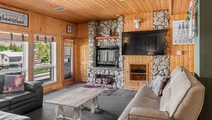 A cozy cabin interior with a stone fireplace, wooden walls, and a television mounted above it. - Aspen Summit Retreat (Brian Head)