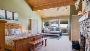 A bedroom with a wooden bed, a bench, a stone fireplace, and a view of the outdoors. - Aspen Summit Retreat (Brian Head)