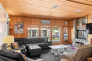 Ein gemütliches Lodge-Interieur mit Holzbalkendecke, Kamin aus Stein, einer schwarzen Ledersofa und einem Schild, das Gäste in die Winterlandschaft willkommen heißt.