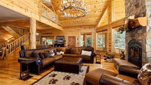 A log cabin interior with a wooden staircase, a fireplace, and a large chandelier. - Great Escape Retreat! Hot Tub & Fire Pit! (Kane County)
