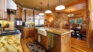 A rustic cabin interior with wooden walls, a kitchen with stainless steel appliances, a dining area with a chandelier, and a staircase. - Great Escape Retreat! Hot Tub & Fire Pit! (Kane County)