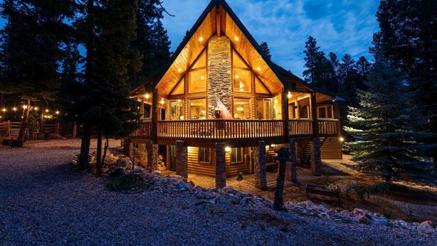 A log cabin with a stone fireplace, a balcony, and a gravel driveway surrounded by trees. - Great Escape Retreat! Hot Tub & Fire Pit! (Kane County)