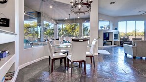 Un comedor amplio con una mesa de vidrio y sillas blancas, un candelabro y vistas al exterior.