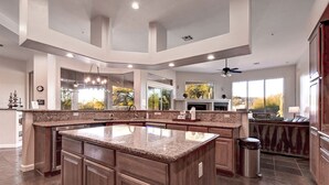 Una cocina amplia con una isla grande, armarios de madera oscura y vistas al exterior a través de ventanas amplias.