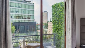 Et soveværelse med en stor skydedør, der fører ud til en balkon med udsigt over en moderne bygning og grøntområde.