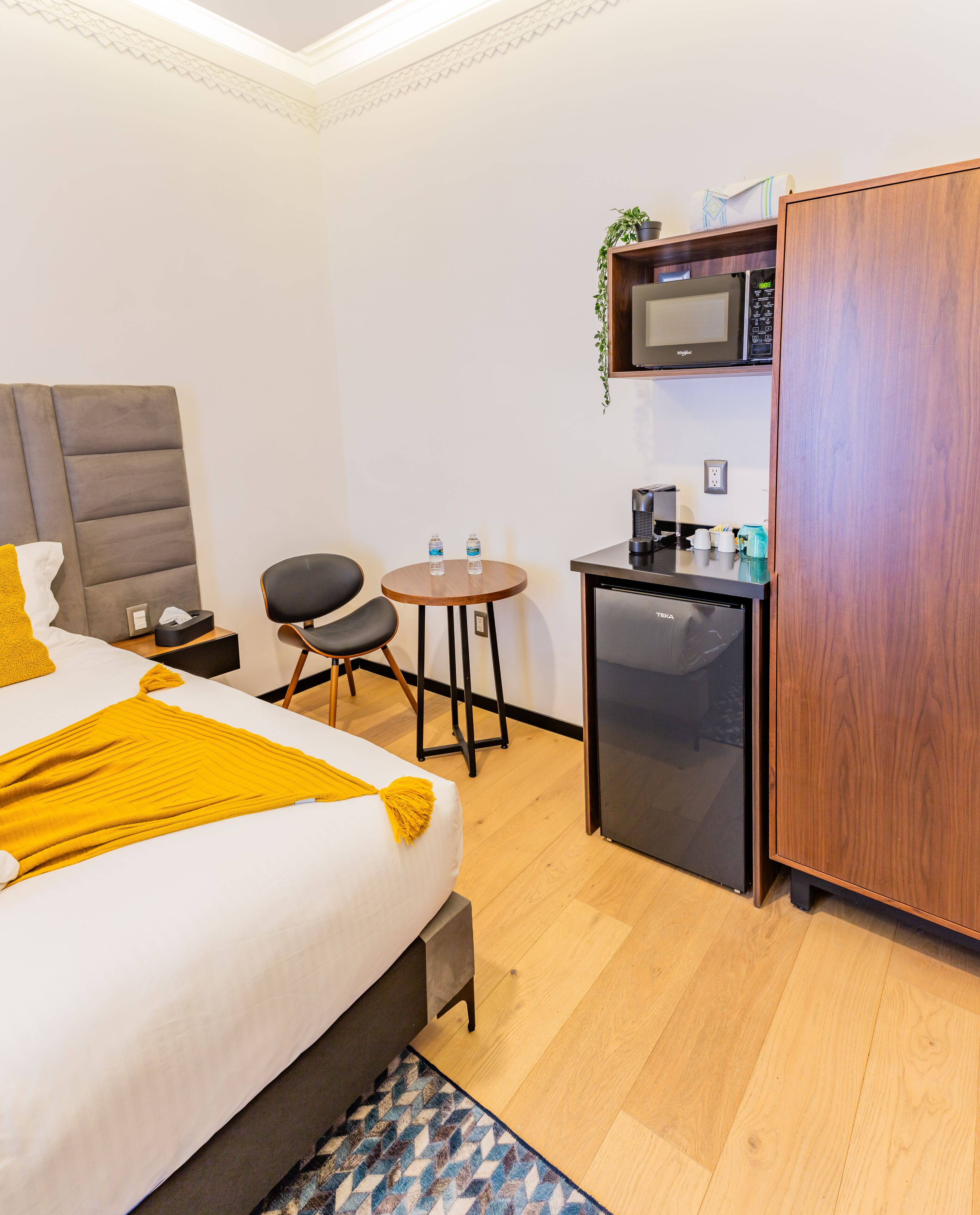 A hotel room with a bed, a small kitchenette, a desk, and a chair.