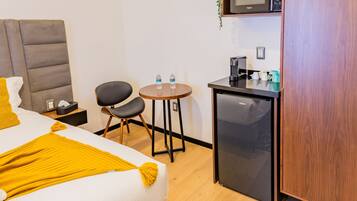 A hotel room with a bed, a small kitchenette, a desk, and a chair.