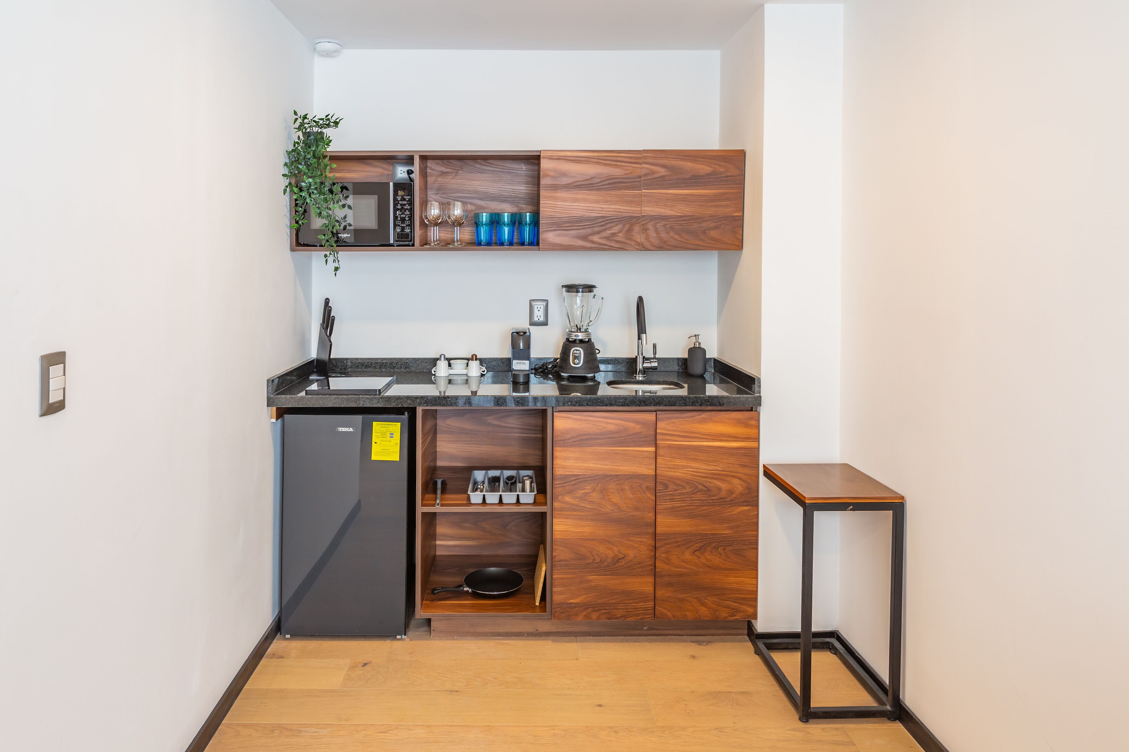 Una cocina compacta con armarios de madera, un microondas integrado y un refrigerador pequeño.