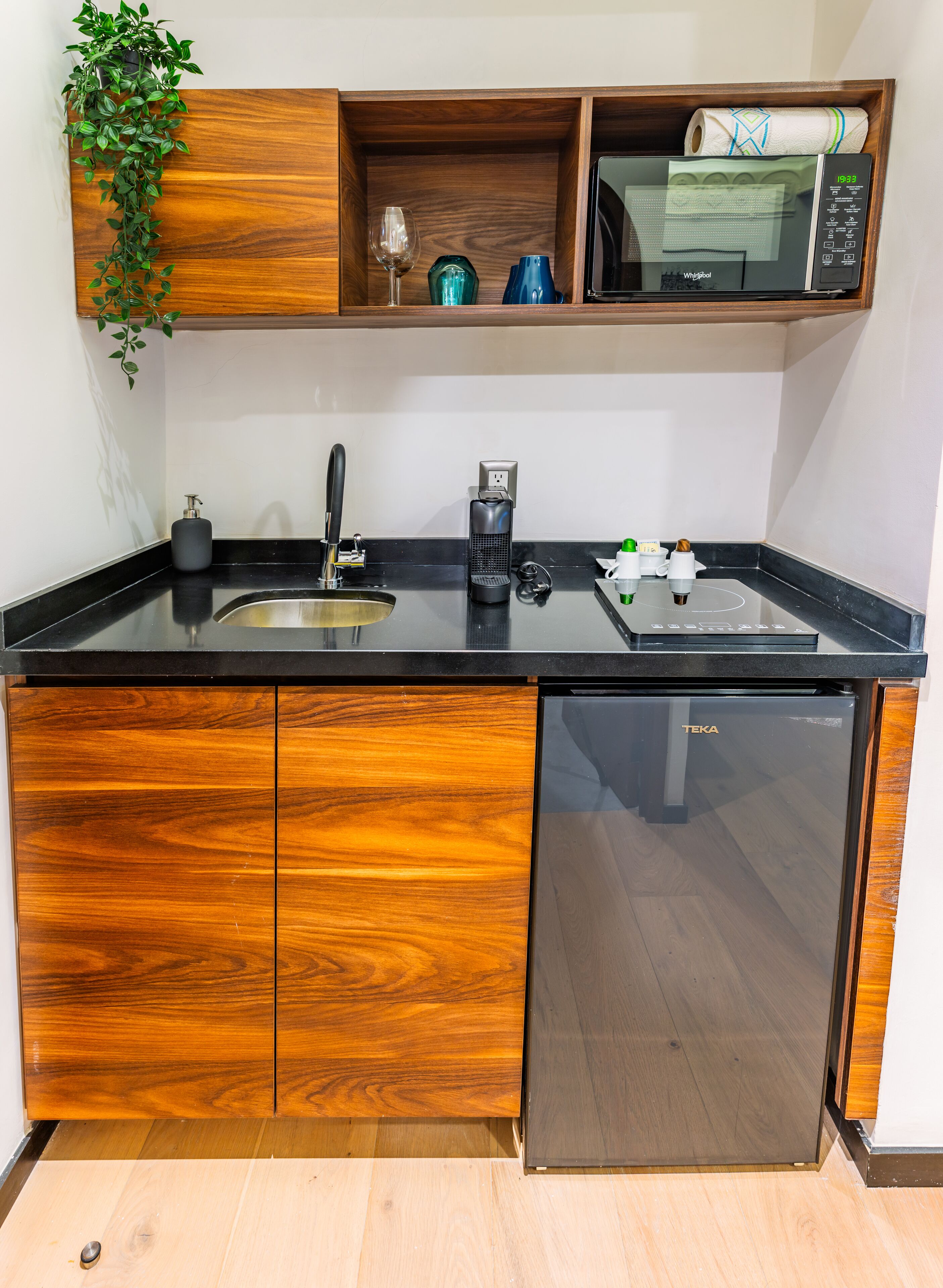 Una cocina con encimera negra, armarios de madera, microondas integrado, cafetera y un lavabo.
