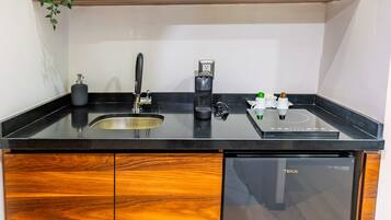Una cocina con encimera negra, armarios de madera, microondas integrado, cafetera y un lavabo.