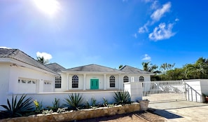 A white building with a green door, arched windows, and a white fence.