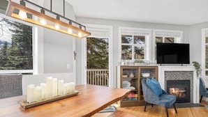 Ein modernes Wohnzimmer mit einem Holztisch, Kerzen, einem blauen Sessel, einem Kamin und einem darüber montierten Fernseher.