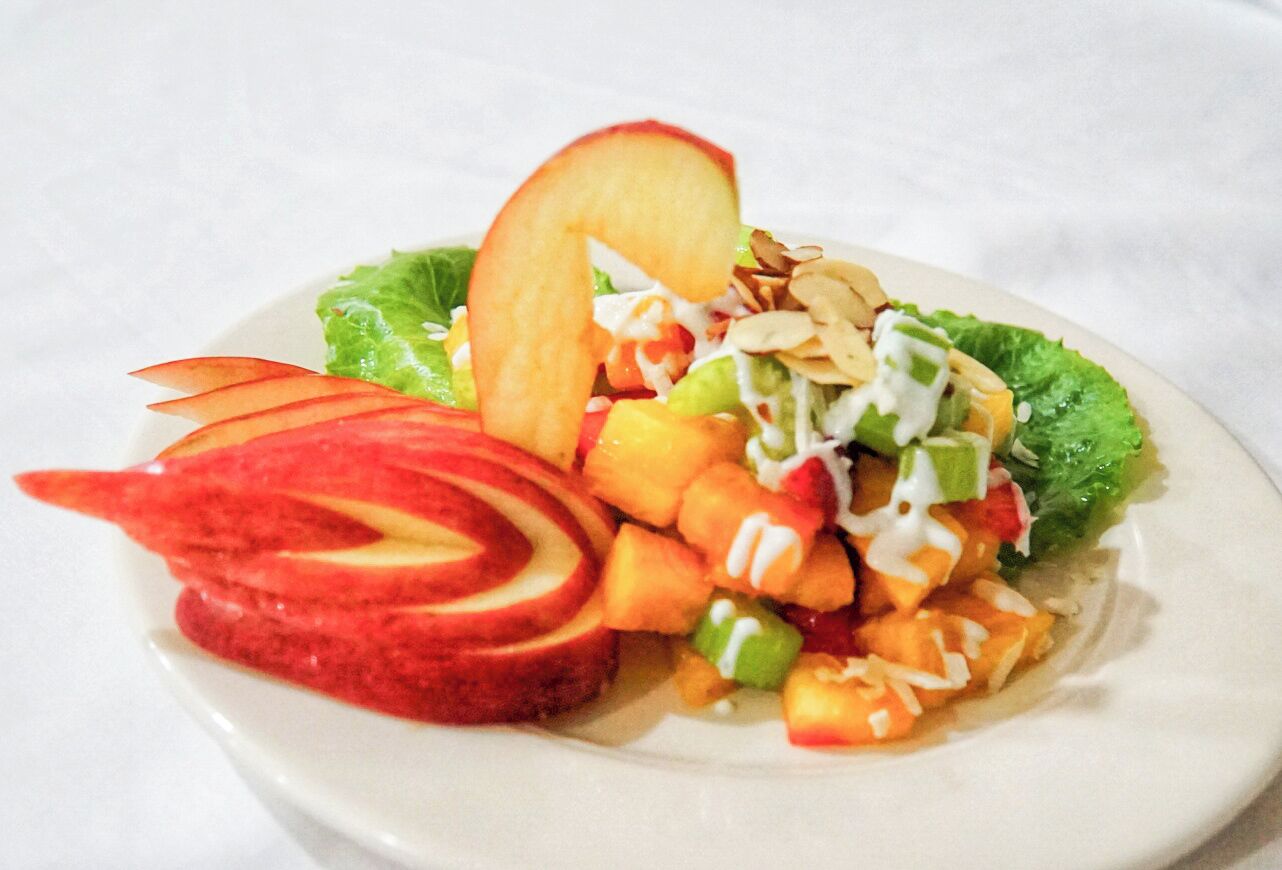 A plate with a fruit salad, including apple slices, peaches, and a dollop of cream.