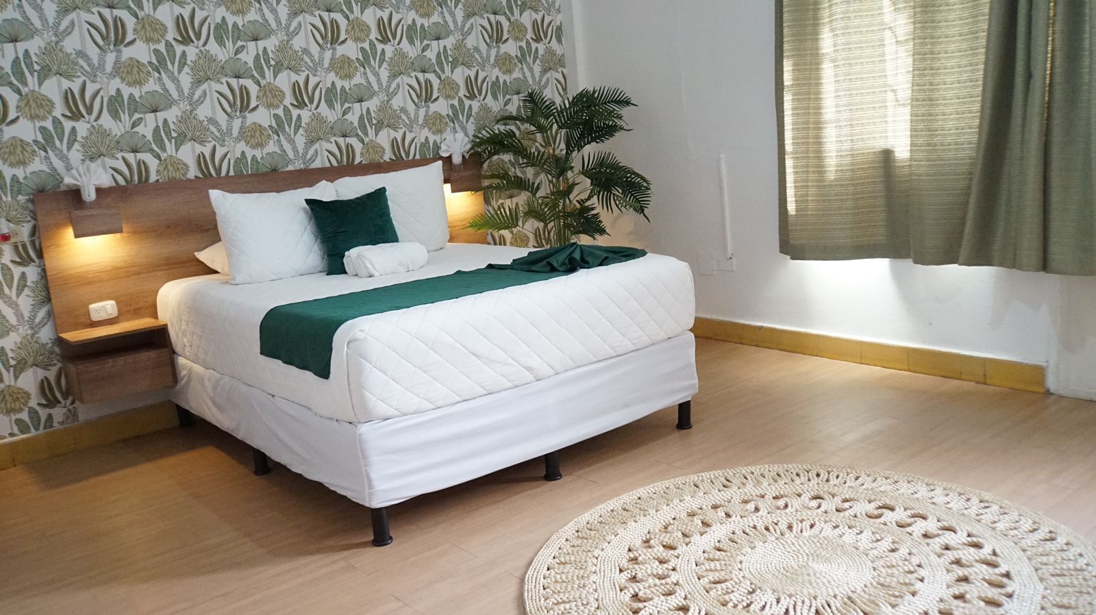 A bedroom with a bed, bedside tables, a potted plant, and a round woven rug.