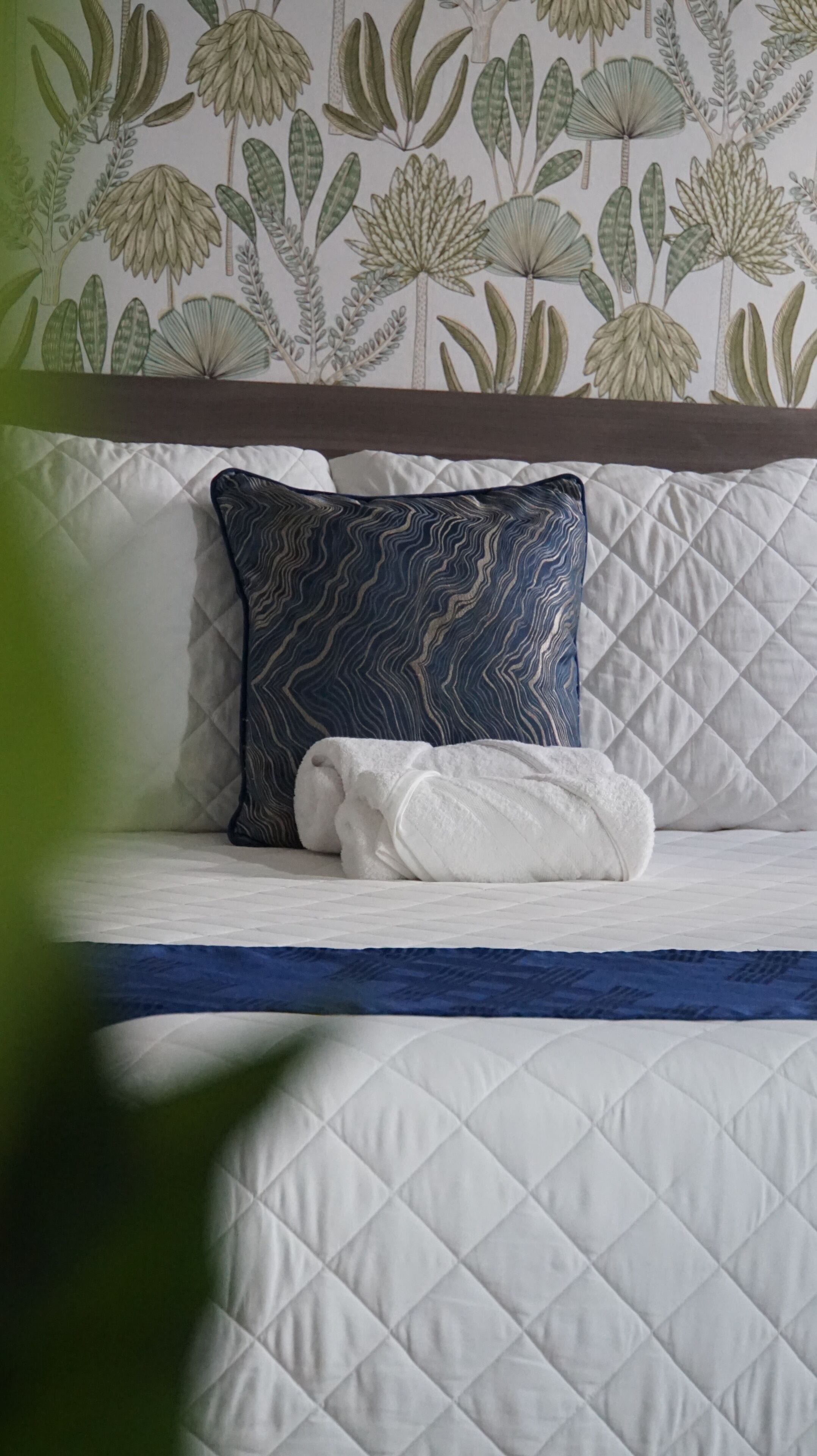 A bed with a quilted white cover, a blue and white patterned pillow, and a white towel.