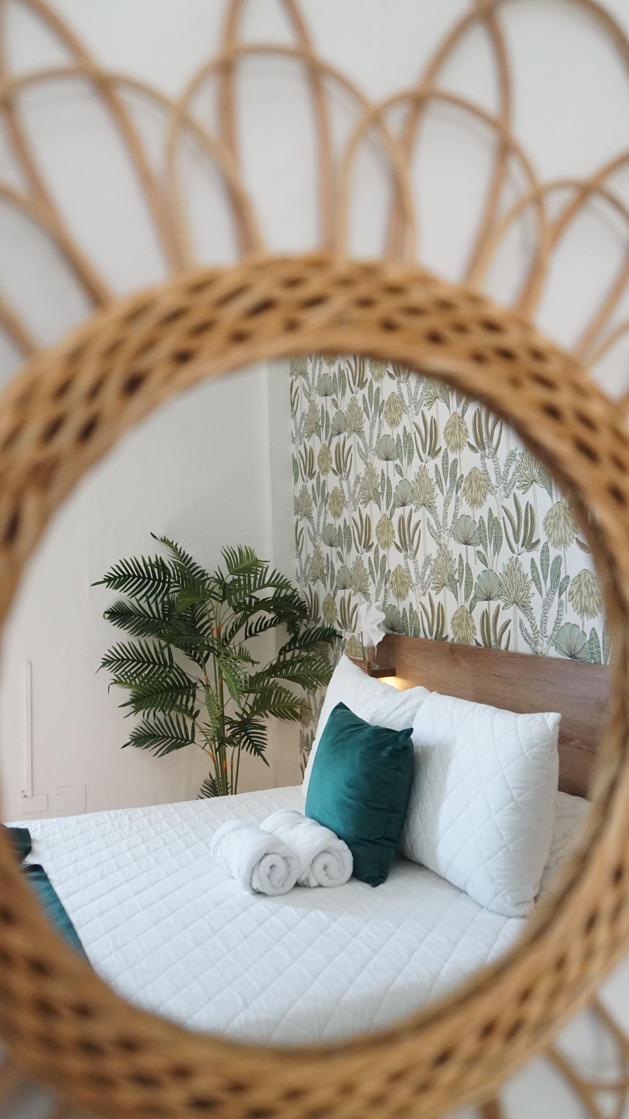 A bed with white bedding, a green pillow, and rolled towels.
