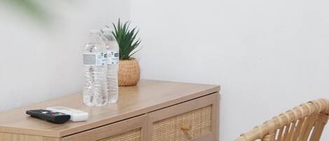 A wicker chair, a wooden table with a remote control, two water bottles, and a small potted plant.