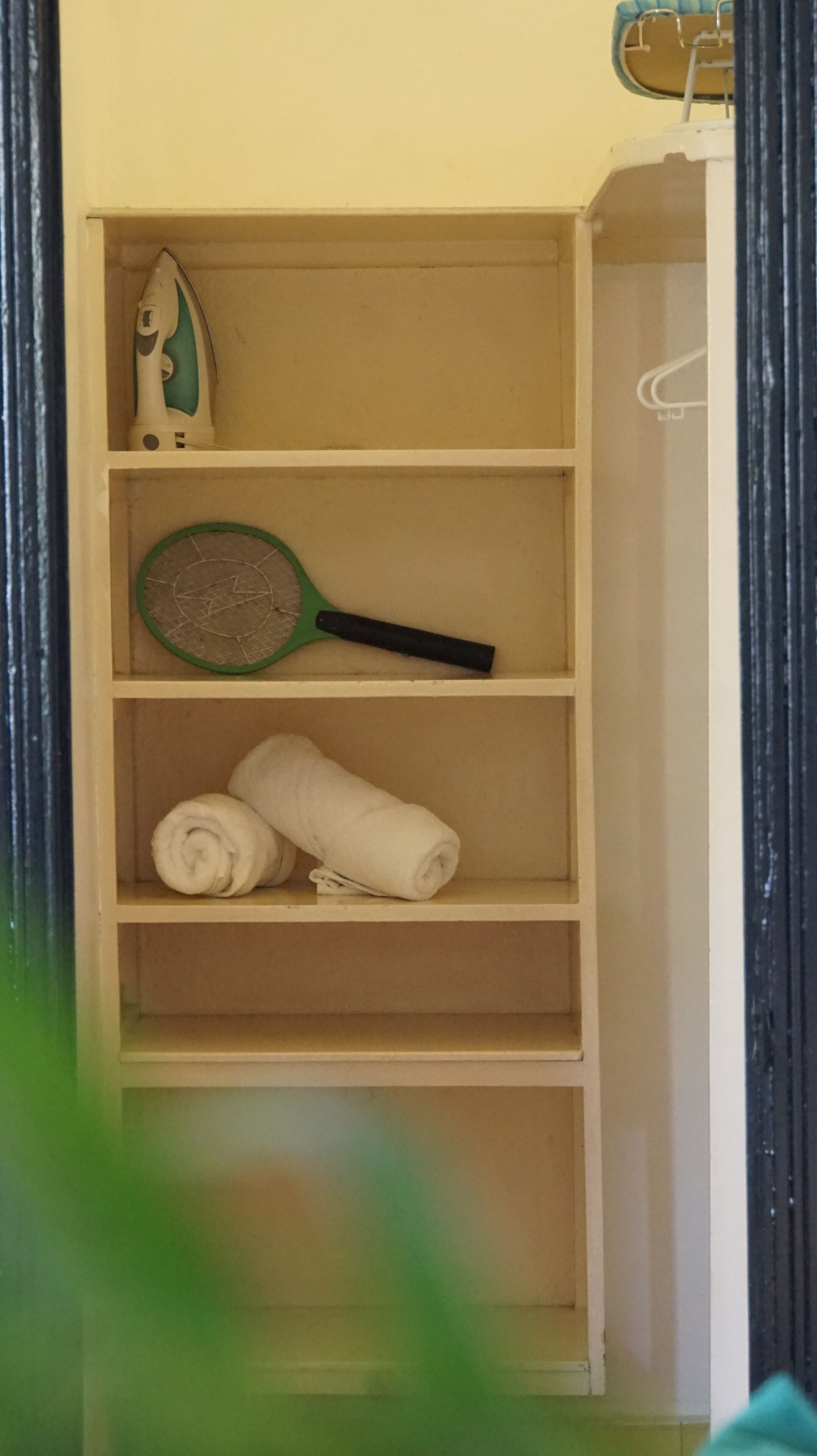 A storage closet with shelves containing a hairdryer, a green-handled paddle, and rolled towels.