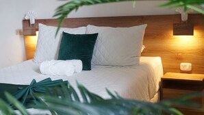 A neatly made bed with white and green pillows, a white bathrobe, and a wooden headboard. - Kali Hotel  (Santa Ana)
