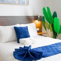 Una cama bien hecha con ropa de cama blanca y azul, un cabecero de madera y una planta verde a su lado.