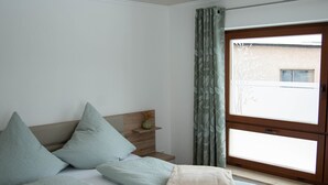 A modern bedroom with a large bed, a nightstand, and a window with curtains. - Cozy holiday home in the heart of the Ore Mountains. (Sehmatal)