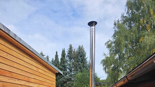 A wooden hot tub with a metal chimney, surrounded by a wooden deck and a small wooden bench. - Cozy holiday home in the heart of the Ore Mountains. (Sehmatal)