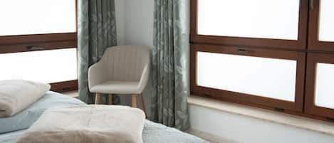 A bedroom with a bed, a chair, and large windows.
