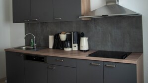 A modern kitchen with dark cabinets, a stainless steel range hood, a sink, and a coffee maker. - Cozy holiday home in the heart of the Ore Mountains. (Sehmatal)