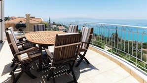A balcony with a wooden table and chairs, a grill, and a view of the sea. - Stunning, Beautiful Villa. Breathtaking Sea Views. Sandy Beaches (Lourdata)