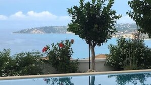 A clear view of a swimming pool with a reflection of the surrounding landscape, including trees and a distant shoreline. - Stunning, Beautiful Villa. Breathtaking Sea Views. Sandy Beaches (Lourdata)