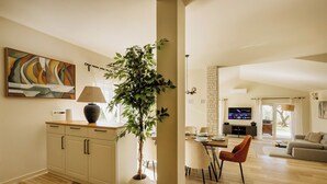Ein modernes Wohnzimmer mit Essbereich, einer großen Pflanze und einem an der Wand befestigten Fernseher.