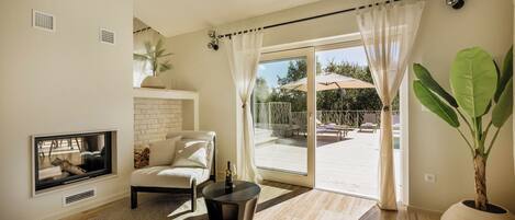A modern living room with a fireplace, comfortable seating, a large window, and a view of an outdoor pool area.