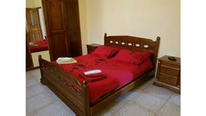 A wooden bed with a red bedspread and matching pillows, a nightstand with a remote control, and a wooden wardrobe. - Exceptional view + large apartment overlooking the Bay of Algiers (Wilaya d'Alger)