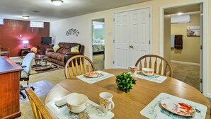 A dining area with a wooden table, chairs, and a small green plant. There is a television in the background and a door leading to another room. - Shared Patio & Fire Pit: Denver Apartment (Denver)