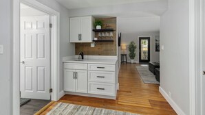 Una cocina moderna con armarios blancos, un revestimiento de pared de madera y una estantería empotrada con copas.