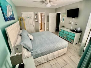 A bedroom with a bed, dresser, TV, and artwork.