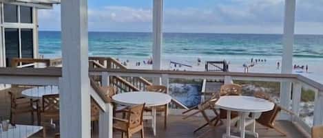A covered outdoor area with wooden tables and chairs, overlooking a beach.