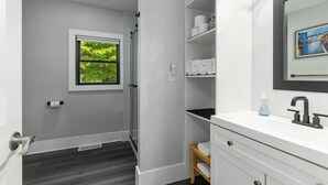 A bathroom with a white vanity, a mirror, a towel rack, and a window with a view of greenery. - Perfect 2-Bedroom Suite in Downtown Saugatuck! (Upper Level Unit) (Saugatuck)