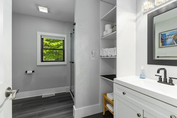 A bathroom with a white vanity, a mirror, a towel rack, and a window with a view of greenery.