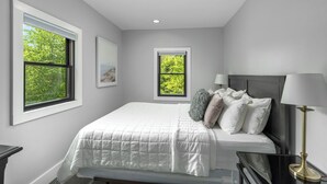 A bedroom with a bed, two windows, a nightstand, and a lamp. - Perfect 2-Bedroom Suite in Downtown Saugatuck! (Upper Level Unit) (Saugatuck)