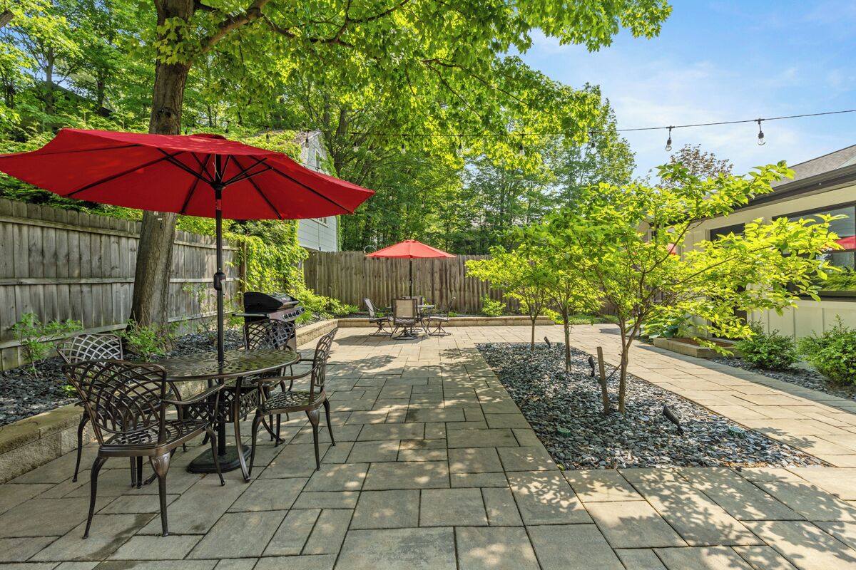 An outdoor patio with a table and chairs, a red umbrella, and a wooden fence.